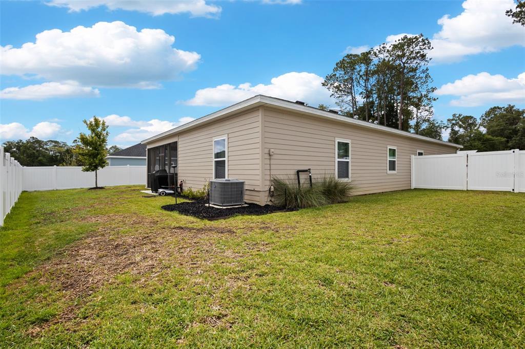 The exterior of a beige house features a screened-in porch, an HVAC unit, and fencing — 560 NW 4TH AVENUE, WILLISTON, FL