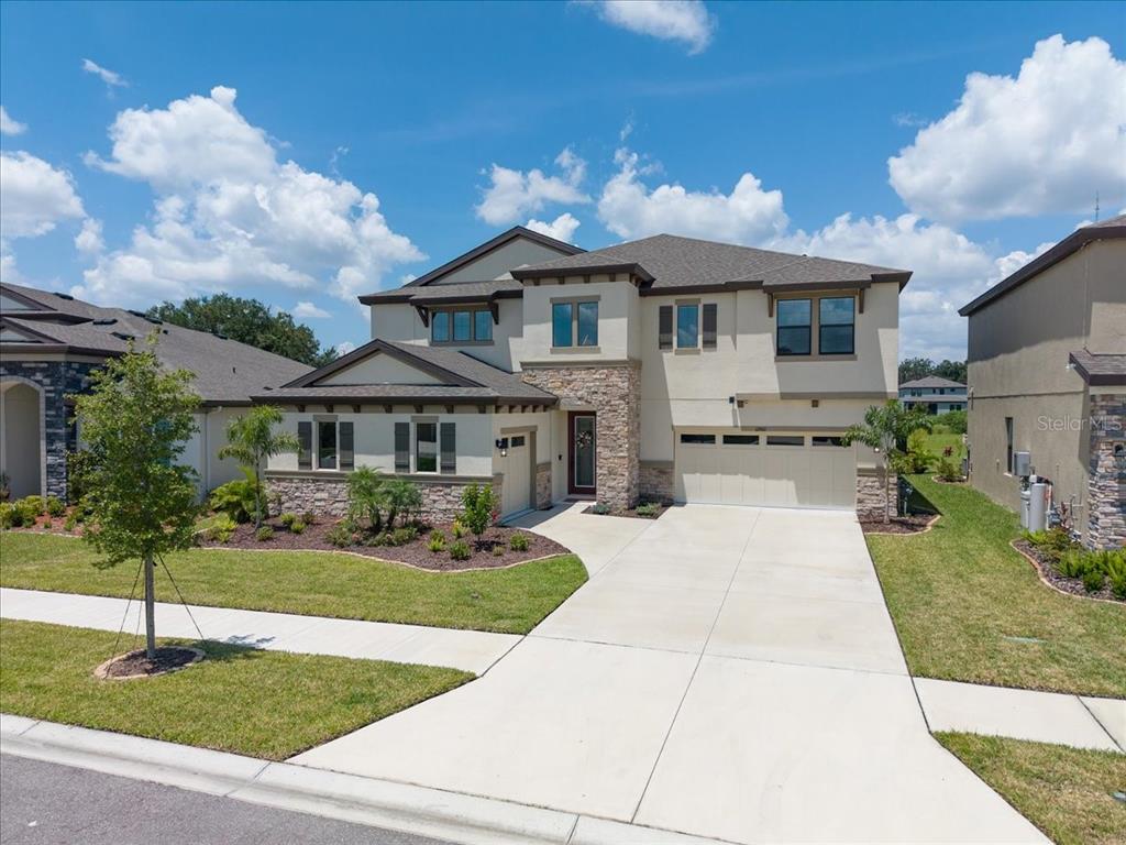 A two-story suburban house with a stone facade, beige stucco, and a concrete driveway — 12962 STEED TRACE LOOP, LITHIA, FL