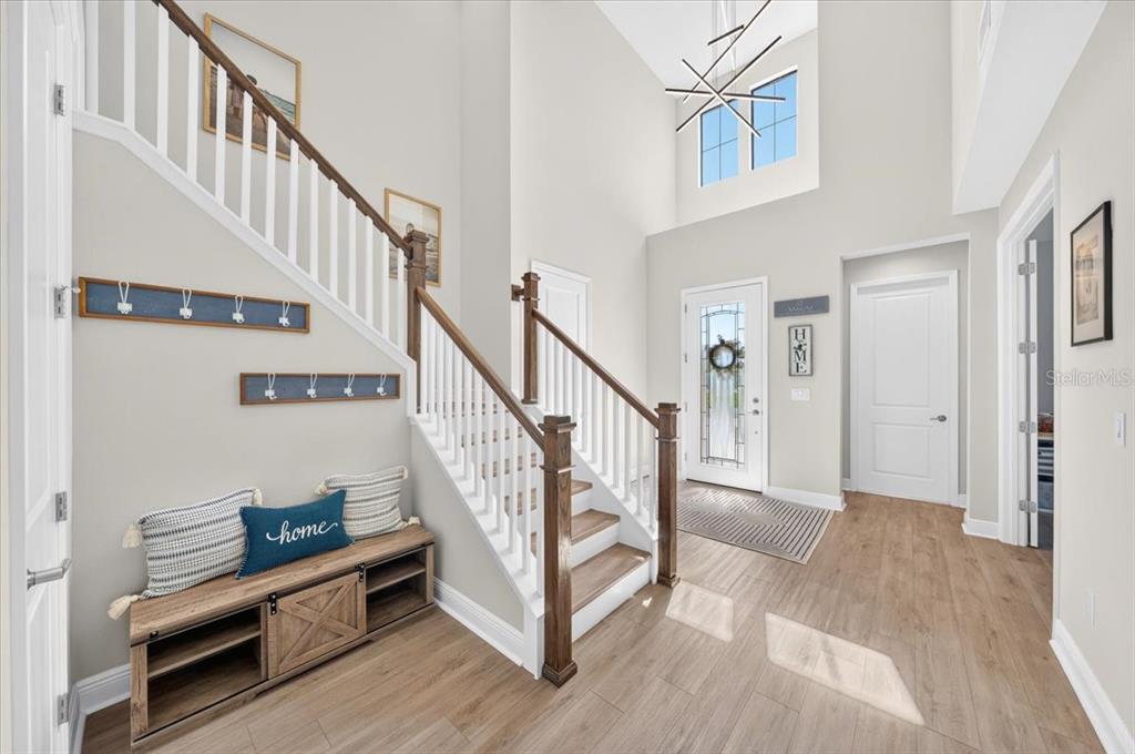 A bright entryway features a wooden staircase, light wood flooring, and a built-in storage bench — 12962 STEED TRACE LOOP, LITHIA, FL