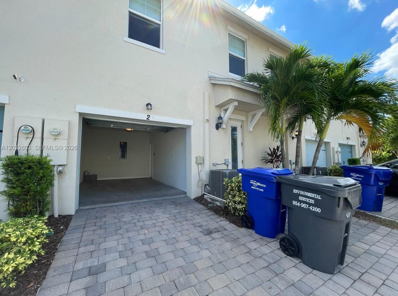 The exterior of a two-story townhouse features a paved driveway, an open garage, and recycling bins — 4920 Eucalyptus Dr # 2, Hollywood FL 33021, HOLLYWOOD, FL