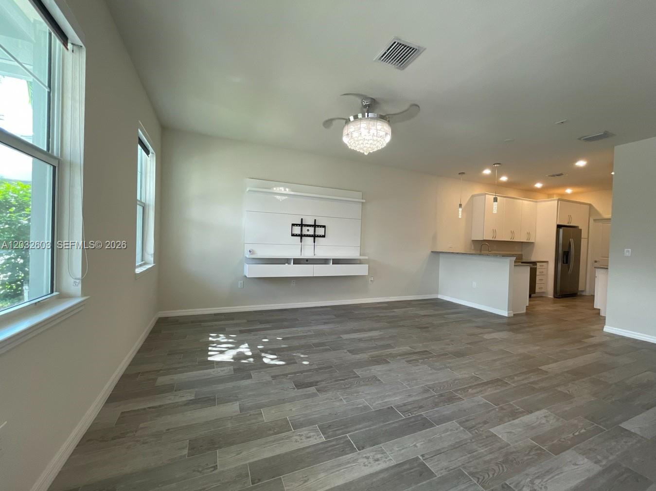 A living room with gray wood-look tile flooring, a wall-mounted media console, and an adjacent kitchen — 4920 Eucalyptus Dr # 2, Hollywood FL 33021, HOLLYWOOD, FL
