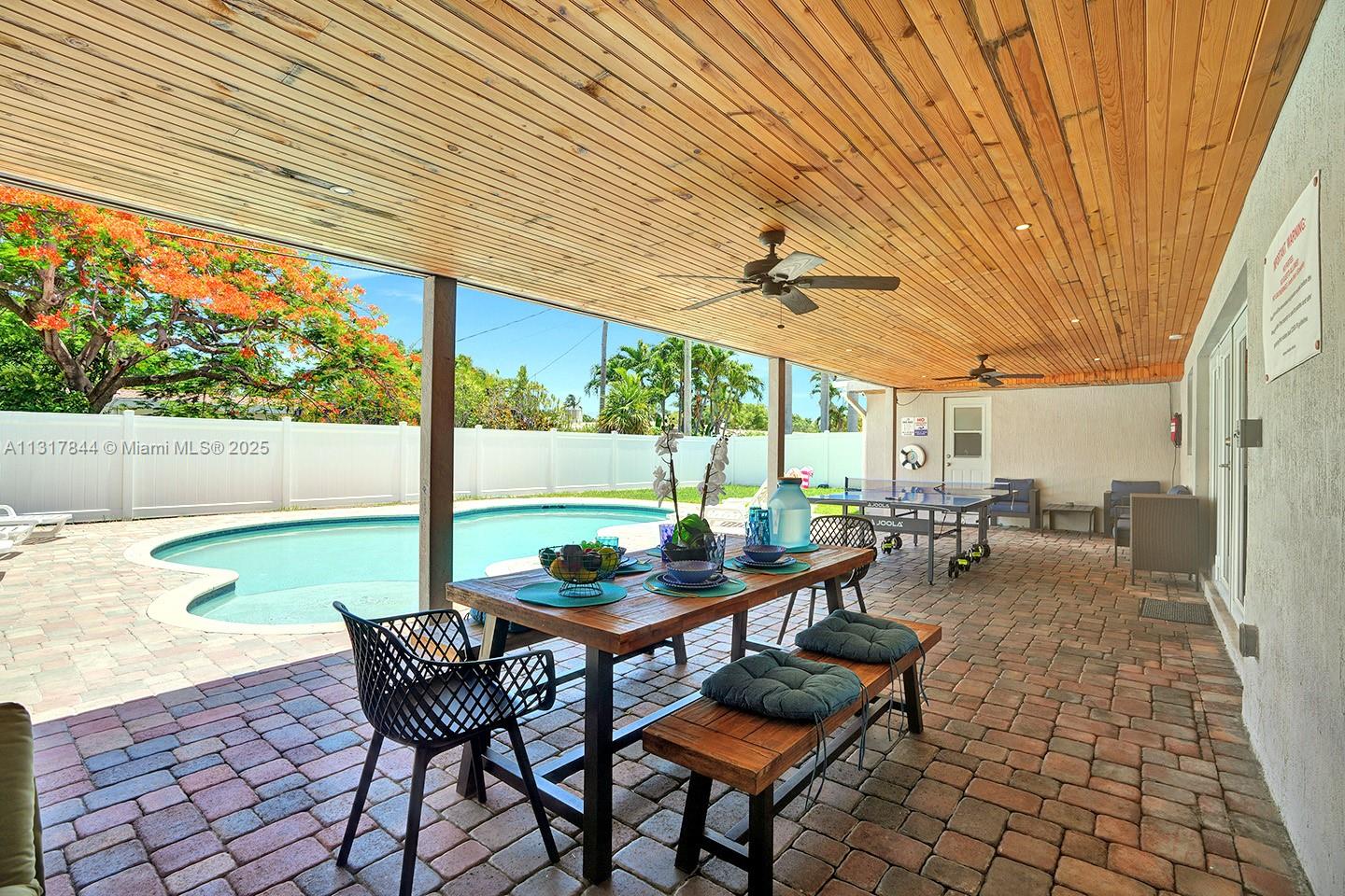 A covered patio features a dining set, ping pong table, and pool overlooking a backyard — 1301 Rodman St, Hollywood FL 33019, HOLLYWOOD, FL