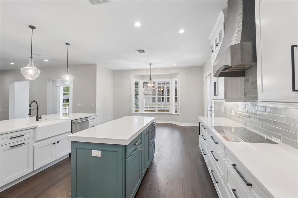 A modern kitchen features white cabinetry, a teal island, quartz countertops, and dark wood flooring — 5105 W NEPTUNE WAY, TAMPA, FL