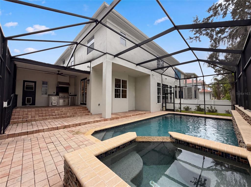 A screened-in patio features a swimming pool, a raised spa, and an outdoor kitchen area — 5105 W NEPTUNE WAY, TAMPA, FL