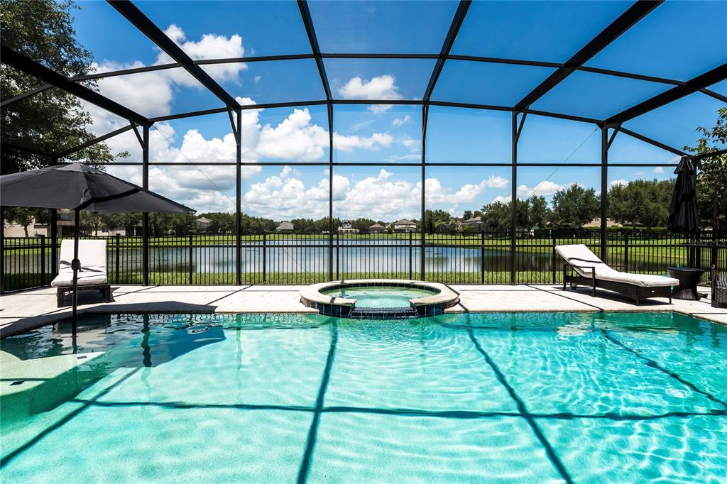A screened-in swimming pool and spa overlook a lake on a sunny day — 11750 CHATEAUBRIAND AVENUE, ORLANDO, FL