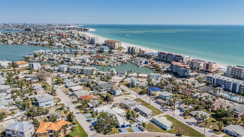 An aerial view shows a coastal neighborhood with houses, apartment buildings, and a sandy beach — 14060 MIRAMAR AVENUE, ST PETERSBURG, FL