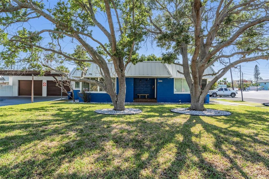 A blue single-story house with a metal roof and two large trees in the yard — 14060 MIRAMAR AVENUE, ST PETERSBURG, FL