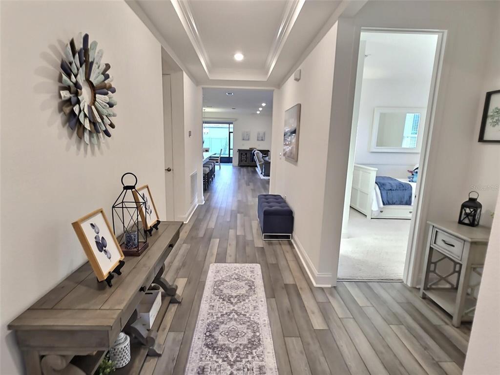 A hallway with wood-look flooring leads to an open living area with a tray ceiling — 2 PAT PLACE, PALM COAST, FL