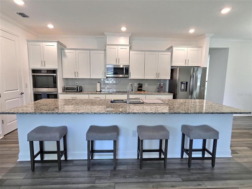 A kitchen features white cabinets, granite countertops, a large island with four stools, and appliances — 2 PAT PLACE, PALM COAST, FL