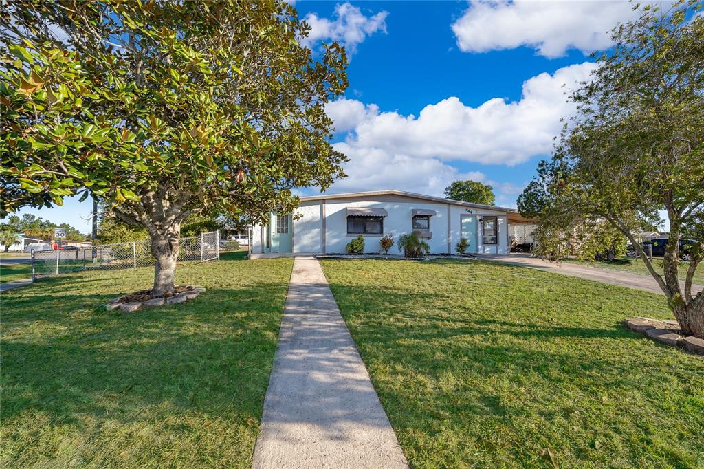 A single-story house with a white exterior, a concrete walkway, and large trees in front — 944 HALSTEAD STREET, DELTONA, FL