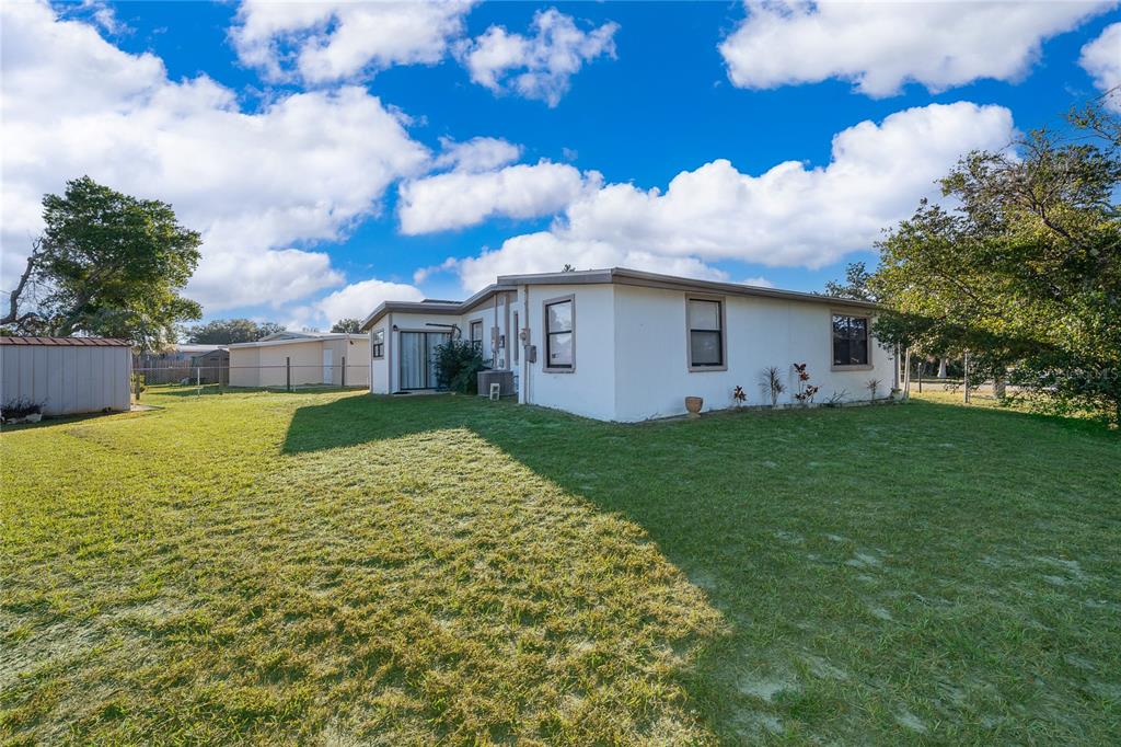 The exterior of a white, single-story house with a large grassy backyard under a blue sky — 944 HALSTEAD STREET, DELTONA, FL