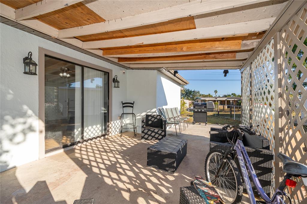 A covered concrete patio features a sliding glass door, outdoor furniture, and a lattice screen — 944 HALSTEAD STREET, DELTONA, FL