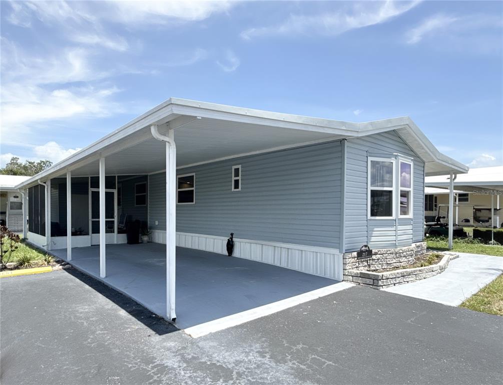 A light blue manufactured home features a large attached carport and a screened-in porch area — 217 MOUNT PINEY AVENUE NE UNIT 286, ST PETERSBURG, FL