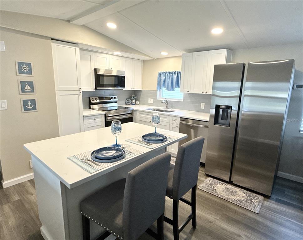 A modern kitchen features white cabinets, stainless steel appliances, and a central island with seating — 217 MOUNT PINEY AVENUE NE UNIT 286, ST PETERSBURG, FL