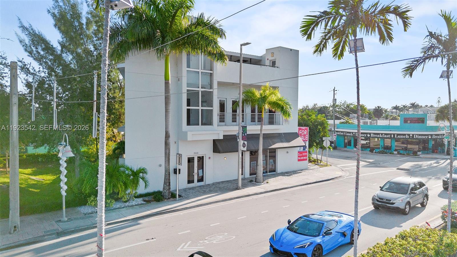 A three-story white commercial building stands on a street corner with a blue sports car — 2500 Wilton Dr, Wilton Manors FL 33305, WILTON MANORS, FL