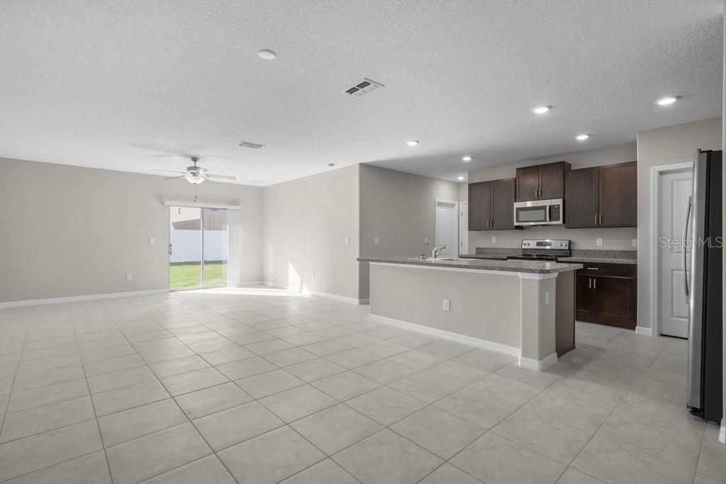 An open-concept kitchen and living area featuring tile flooring, dark cabinetry, and a breakfast bar — 7227 RONNIE GARDENS COURT, TAMPA, FL