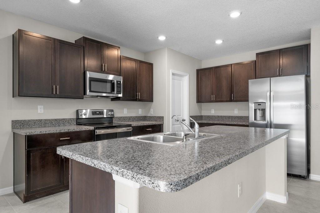 A kitchen features dark wood cabinets, granite countertops, a center island, and stainless steel appliances — 7227 RONNIE GARDENS COURT, TAMPA, FL