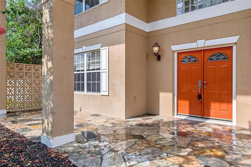 A tan house exterior features a stone patio, a large pillar, and bright orange double doors — 3 ZORRO COURT, PALM COAST, FL