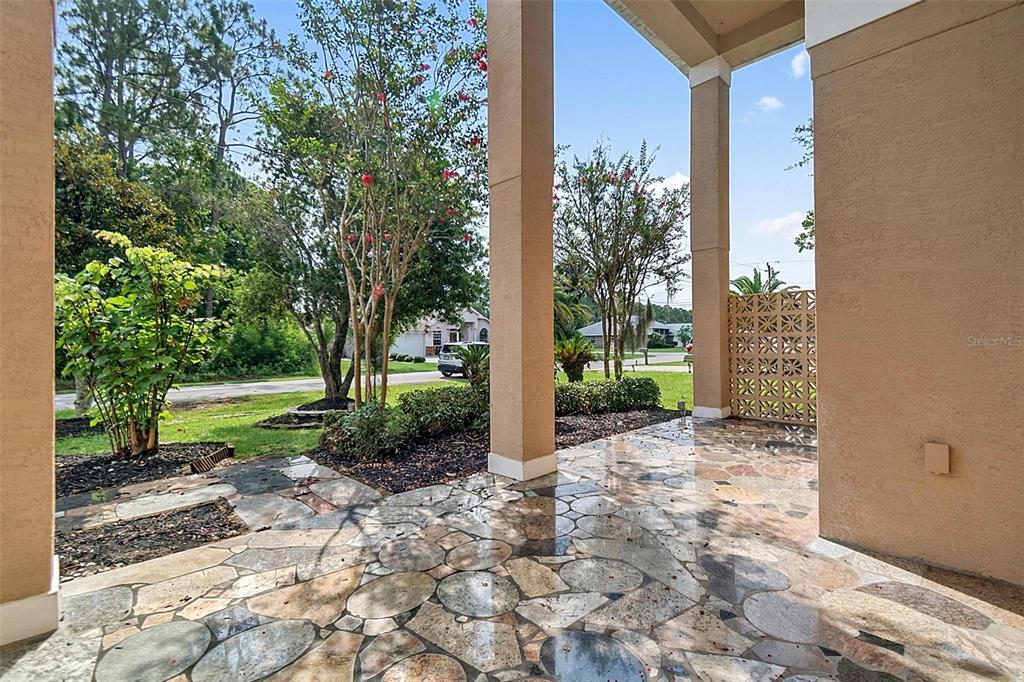 A covered patio features a natural stone floor and square support columns overlooking a yard — 3 ZORRO COURT, PALM COAST, FL