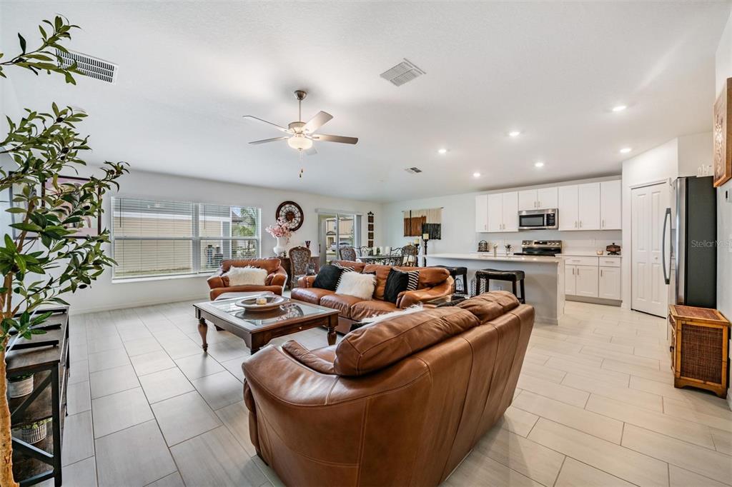 An open-concept living room and kitchen featuring brown leather furniture and light-colored tile flooring — 32325 WISHING HAVEN DRIVE, SAN ANTONIO, FL