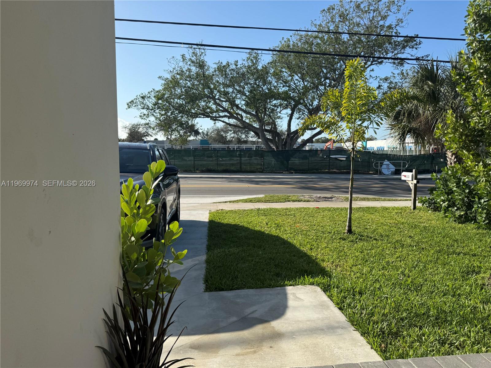 A view from a driveway shows a lawn, a small palm tree, and a road — 413 SW 10th St, Delray Beach FL 33444, DELRAY BEACH, FL