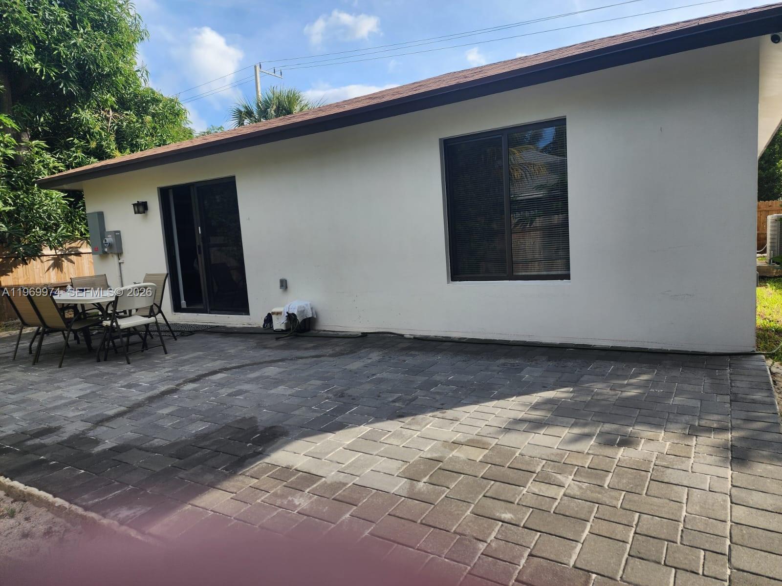 A paved patio sits outside a white house with a sliding door and a window — 413 SW 10th St, Delray Beach FL 33444, DELRAY BEACH, FL