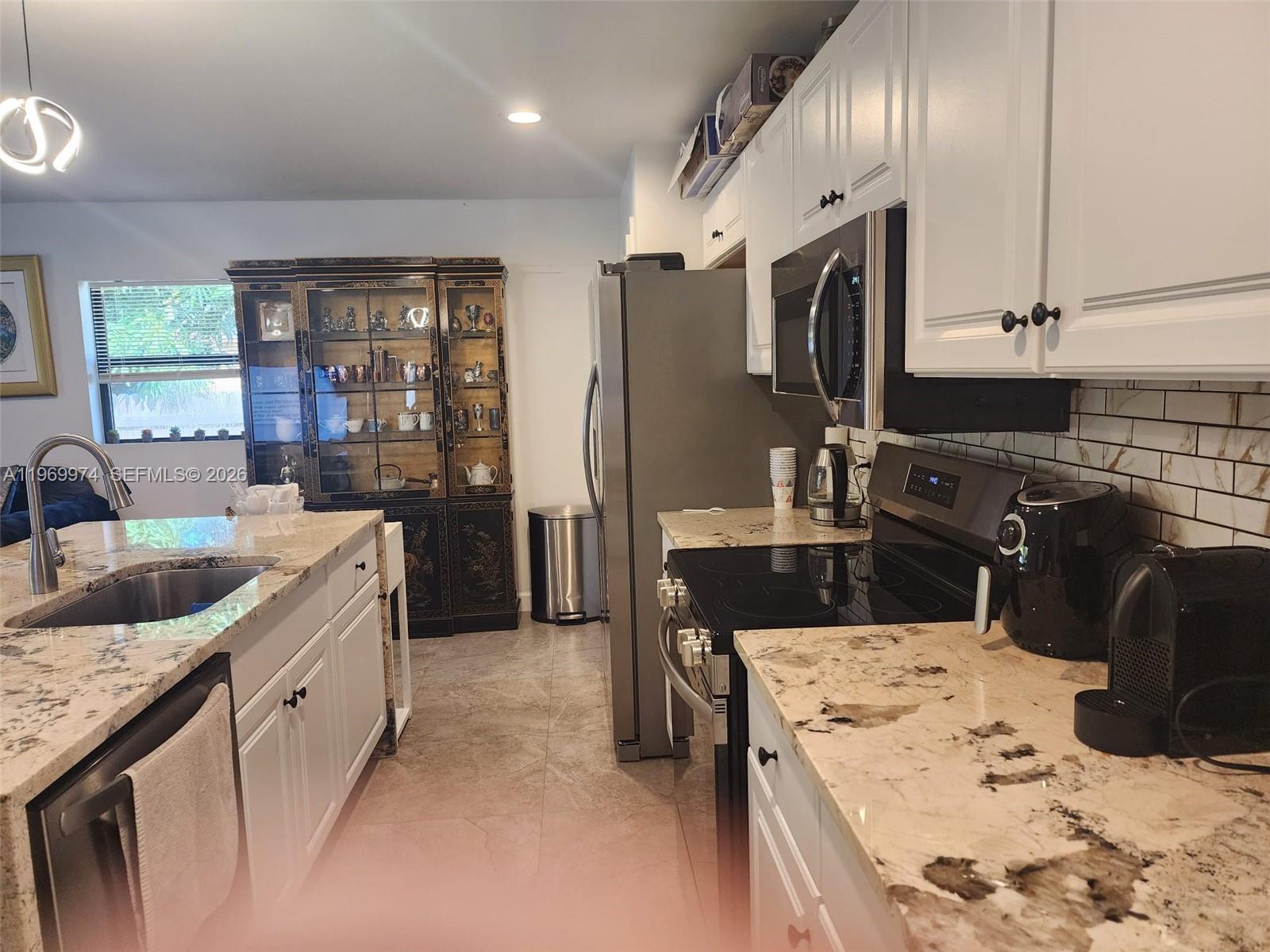 A kitchen features white cabinets, granite countertops, stainless steel appliances, and a dark display cabinet — 413 SW 10th St, Delray Beach FL 33444, DELRAY BEACH, FL