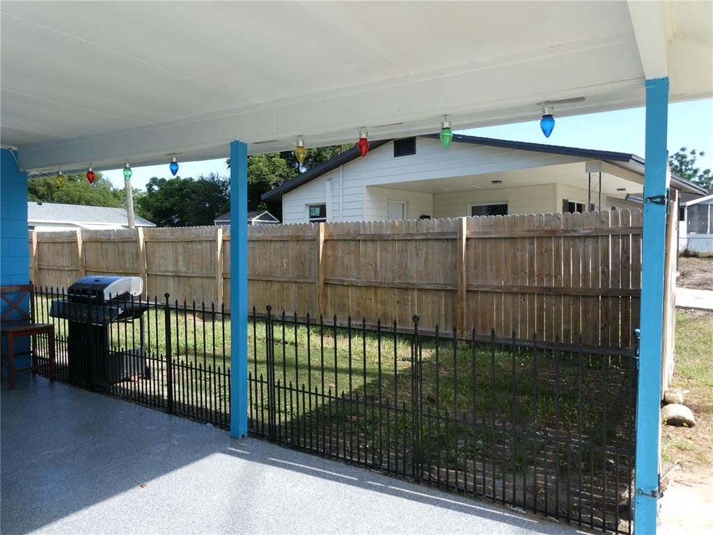 A covered patio features a black metal fence, a grill, and colorful string lights — 2912 DUDLEY DRIVE, BARTOW, FL