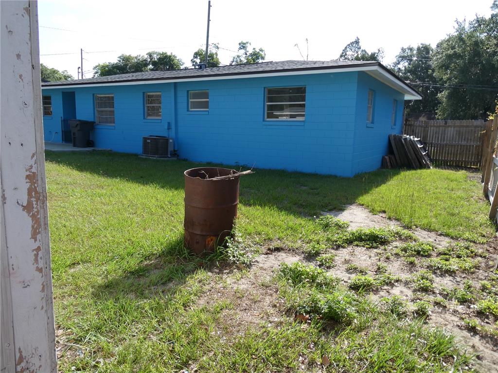 A bright blue concrete block house sits in a grassy backyard with a metal barrel — 2912 DUDLEY DRIVE, BARTOW, FL