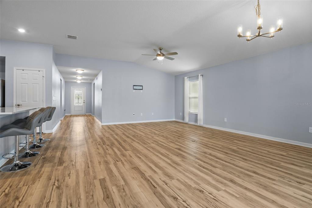 A spacious living area features light blue walls, wood-look flooring, and a breakfast bar — 1591 MATTIE POINTE PLACE, AUBURNDALE, FL