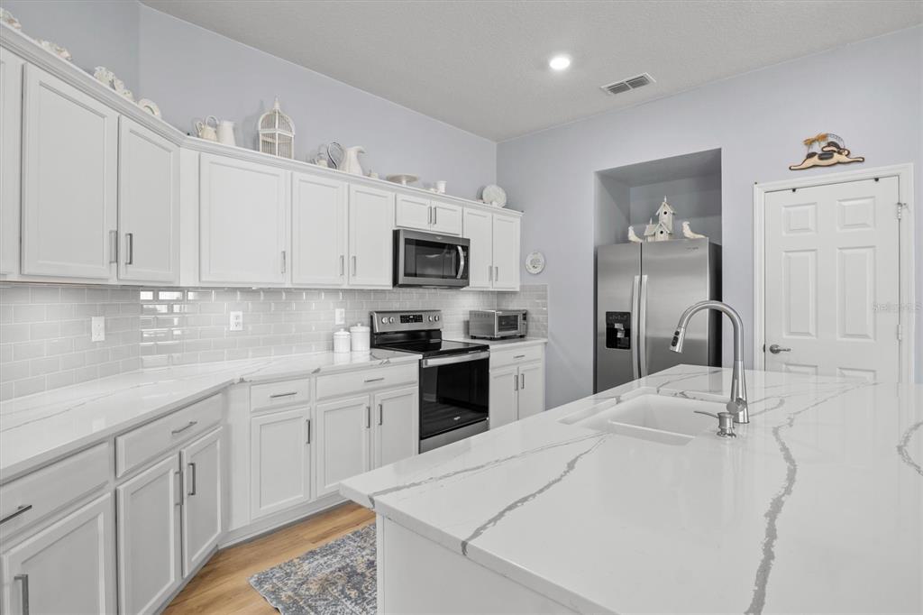 A modern kitchen features white cabinetry, quartz countertops, a center island, and stainless steel appliances — 1591 MATTIE POINTE PLACE, AUBURNDALE, FL