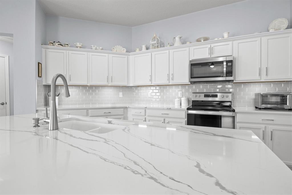 A modern kitchen features white cabinets, a large quartz island, and a subway tile backsplash — 1591 MATTIE POINTE PLACE, AUBURNDALE, FL