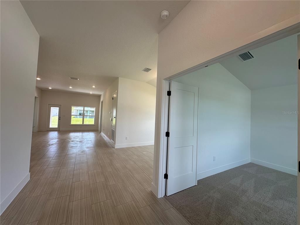 A room with carpet and a white door opens to a tiled living area — 12606 NE 48TH STREET, OXFORD, FL