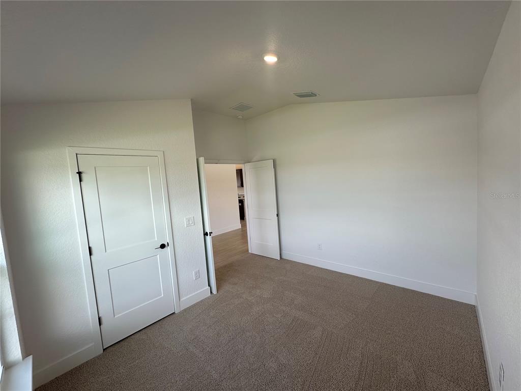 An empty bedroom features beige carpet, white walls, and two white interior doors — 12606 NE 48TH STREET, OXFORD, FL