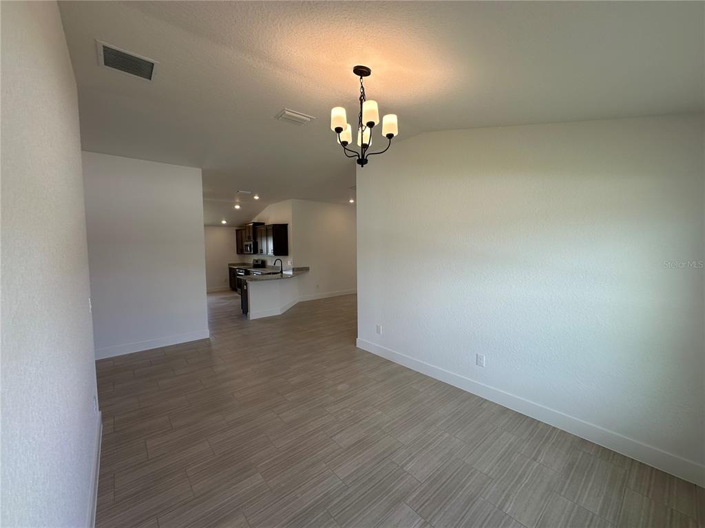 A dining area with tile flooring and a chandelier leads into a kitchen — 12606 NE 48TH STREET, OXFORD, FL