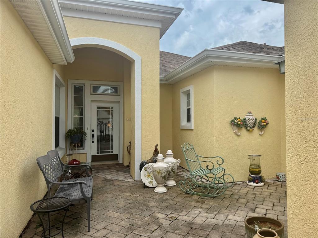A paved courtyard entrance features a front door, a metal bench, and a rocking chair — 12491 SE 91ST TERRACE ROAD, SUMMERFIELD, FL
