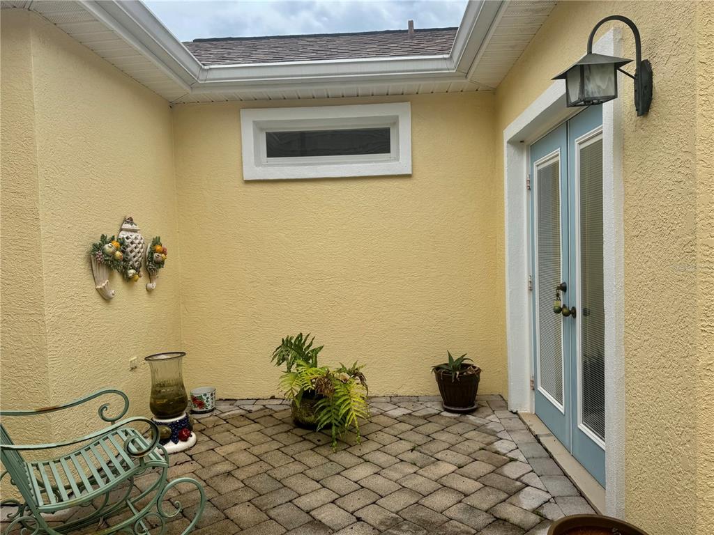 A small outdoor patio with yellow stucco walls, a brick floor, and light blue French doors — 12491 SE 91ST TERRACE ROAD, SUMMERFIELD, FL
