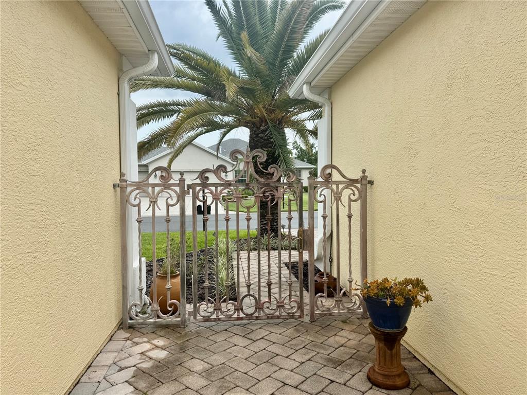 A wrought iron gate stands between two stucco walls on a paved patio area — 12491 SE 91ST TERRACE ROAD, SUMMERFIELD, FL