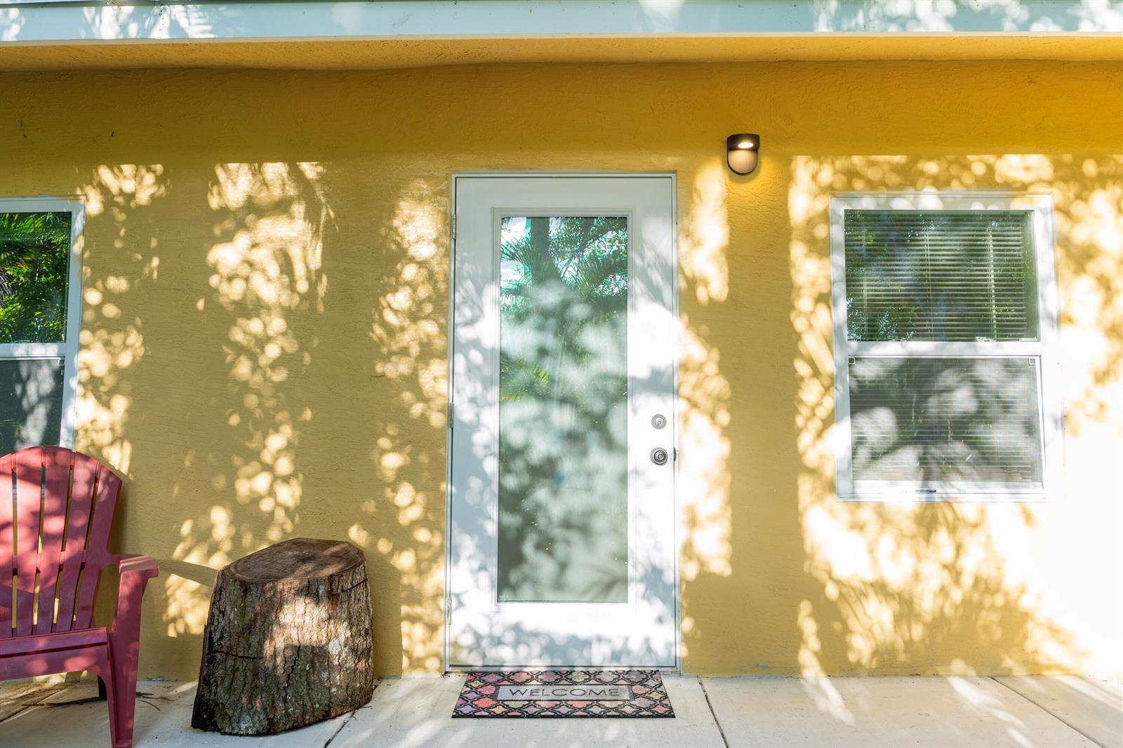 A yellow exterior wall features a central glass door, a window, and a red chair — 13075 Marcella Boulevard Unit 2, FL 33470, FL