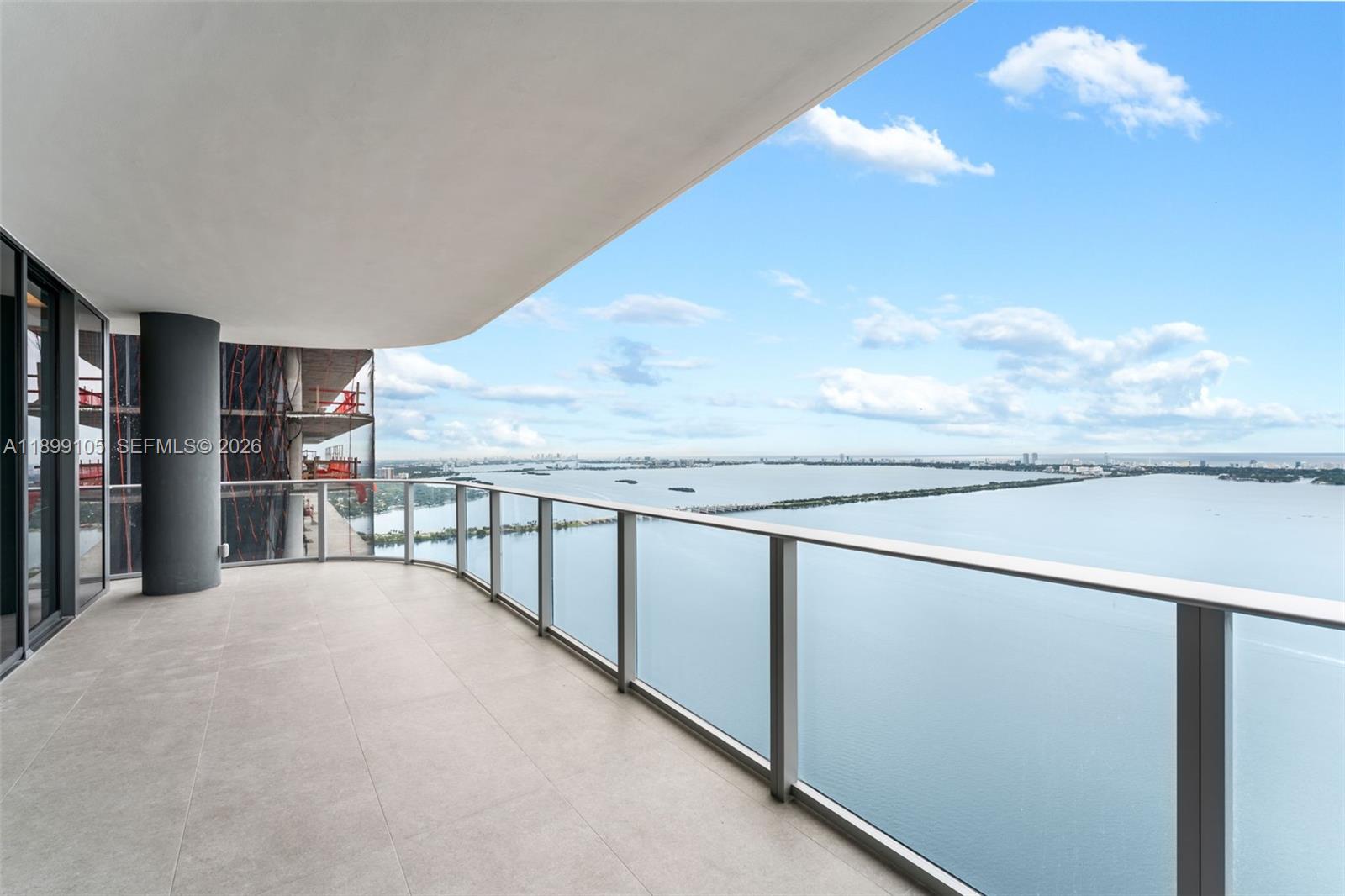 A spacious balcony with glass railings overlooks a large body of water and city skyline — 700 NE 24th St # 5401, Miami FL 33137, MIAMI, FL