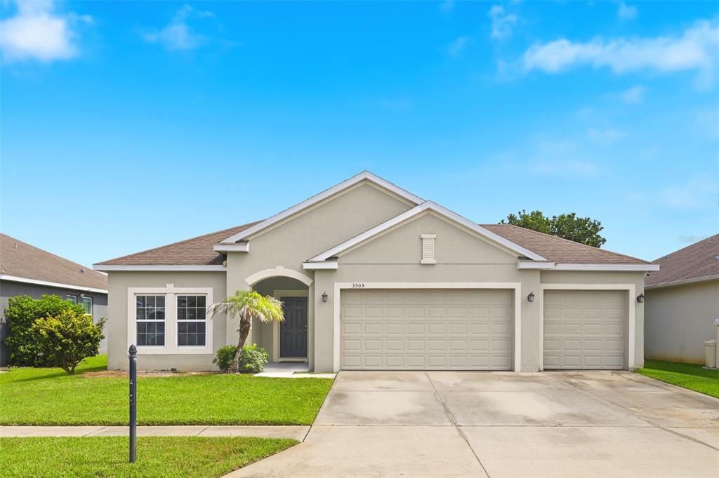 A single-story suburban house with a beige stucco exterior, a two-car garage, and a lawn — 3505 SPRITE LANE, ST CLOUD, FL
