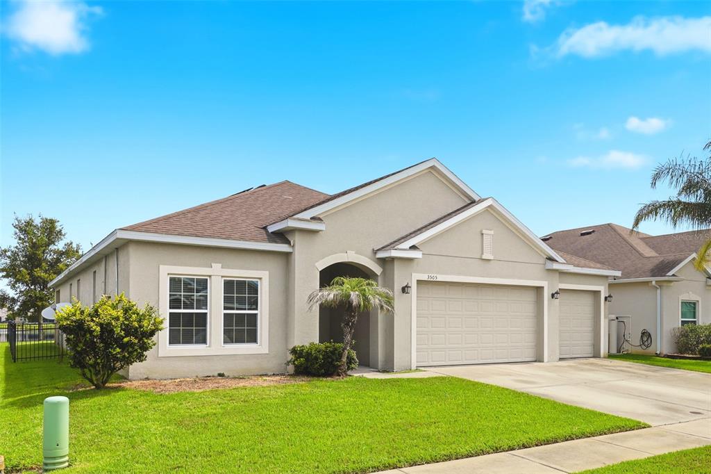 A single-story suburban house with a beige stucco exterior, a two-car garage, and a lawn — 3505 SPRITE LANE, ST CLOUD, FL