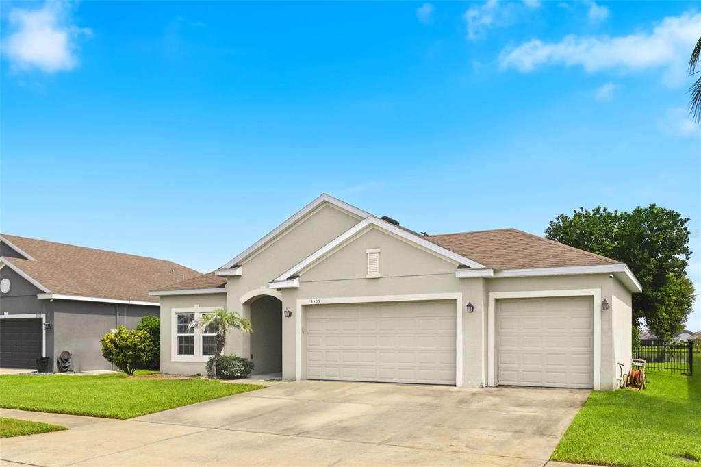 A single-story house with a beige stucco exterior, a three-car garage, and a green lawn — 3505 SPRITE LANE, ST CLOUD, FL