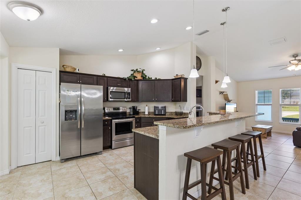 A kitchen features dark wood cabinets, granite countertops, stainless steel appliances, and a breakfast bar — 7042 SE 122ND LANE, BELLEVIEW, FL