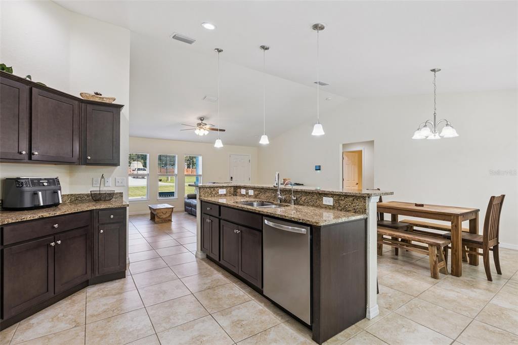 A kitchen with dark wood cabinets, granite countertops, and a dining area in the background — 7042 SE 122ND LANE, BELLEVIEW, FL