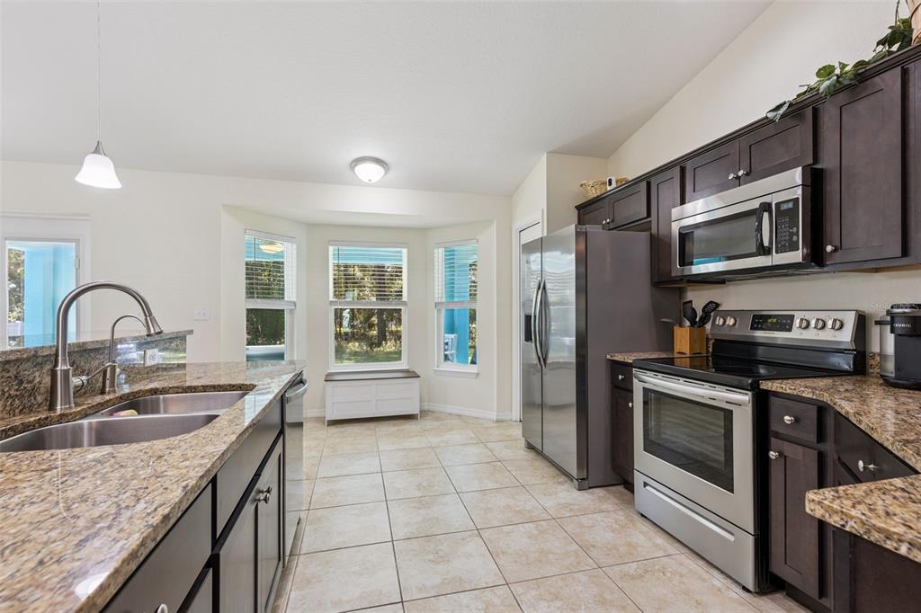 An open-concept kitchen and dining area features dark wood cabinets, stainless appliances, and tile flooring — 7042 SE 122ND LANE, BELLEVIEW, FL