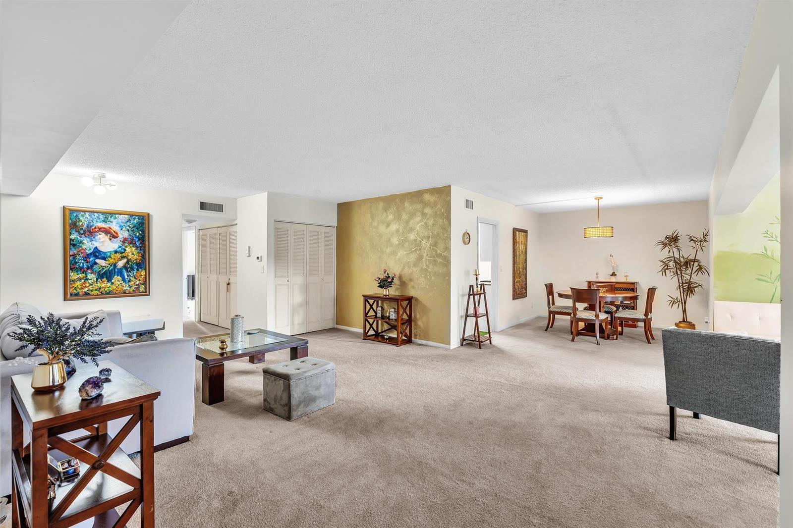 A spacious living and dining area features beige carpeting, a gold accent wall, and furniture — 6561 Spring Bottom Way # 234, Boca Raton FL 33433, BOCA RATON, FL