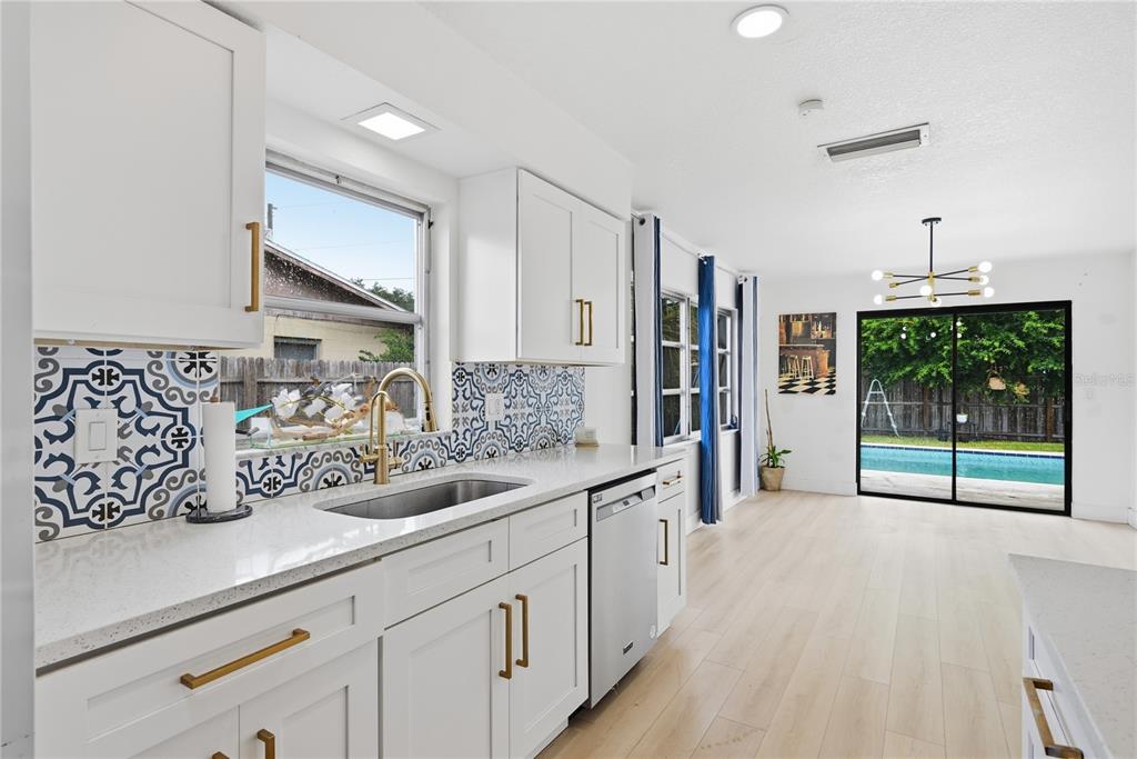 A kitchen with white cabinets, gold hardware, patterned tile backsplash, and a view of a pool — 835 MARLOWE, ORLANDO, FL