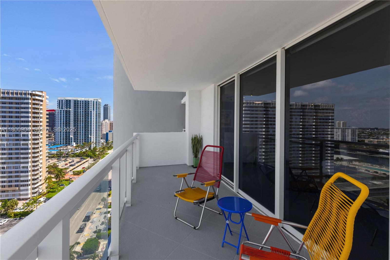 A balcony with two colorful chairs, a small blue table, and views of city buildings — 2030 S Ocean Dr # 1707, Hallandale Beach FL 33009, HALLANDALE BEACH, FL