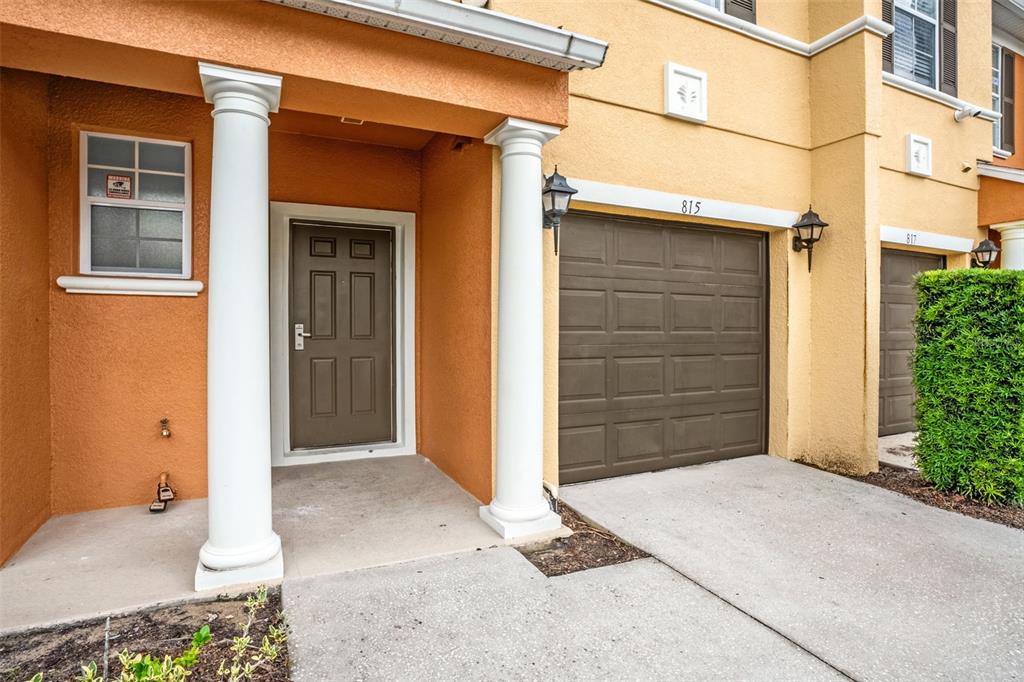 An exterior view of a townhouse entrance with a brown door, garage, and white columns — 815 ASSEMBLY COURT, KISSIMMEE, FL